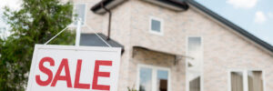 close up shot of wooden placard with sale sign in front of modern cottage