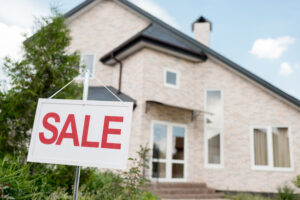 close up shot of wooden placard with sale sign in front of modern cottage