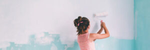 Preteen child painting the wall in her room in blue and white colors. Young girl making interior renovation at home.