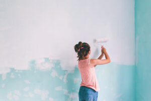 Preteen child painting the wall in her room in blue and white colors. Young girl making interior renovation at home.