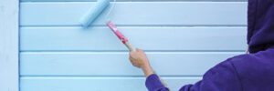 Woman using paint roller to paint wall in blue paint