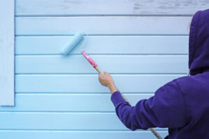 Woman using paint roller to paint wall in blue paint