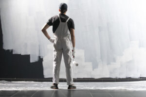 A male painter in uniform, looks at the wall holding a construction roller