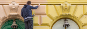 A painter painting an old facade with a brush from yellow to orange on a ladder in Vienna