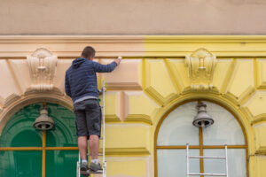 A painter painting an old facade with a brush from yellow to orange on a ladder in Vienna