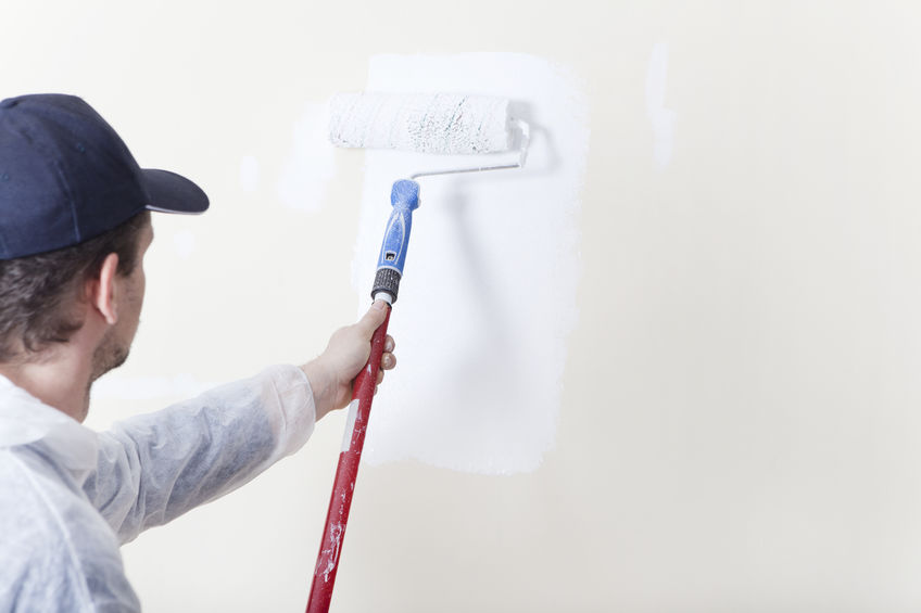 Painter paints an old wall with a paint roller in white