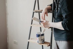 person standing near stepladder holding paintbrush in hand. home renovation concept